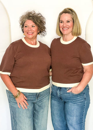 two women modeling a brown, short sleeve sweater with cream banding on sleeves, collar and hem.