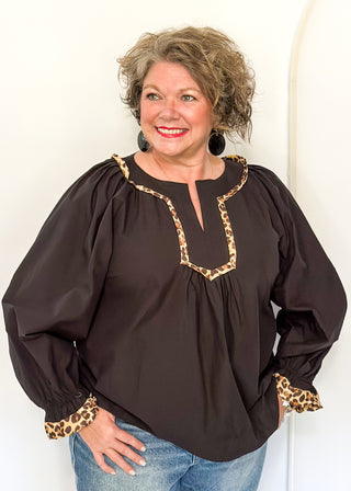Black long-sleeve blouse with leopard print trim on split neckline and cuffs.