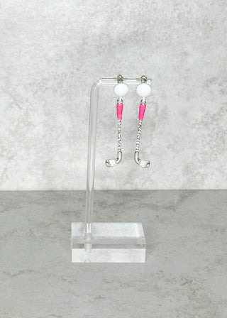 Pair of golf club shaped post back earrings on a clear stand against a gray marble background