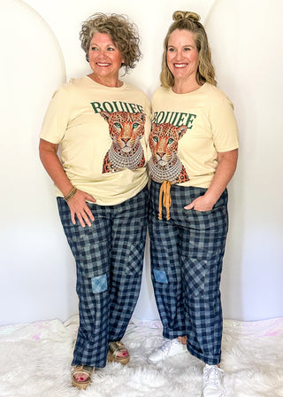 Two women standing side-by-side wearing matching beige graphic t-shirts with a cheetah print and the word 'ROUFE' in green, paired with blue and gray plaid pajama pants.