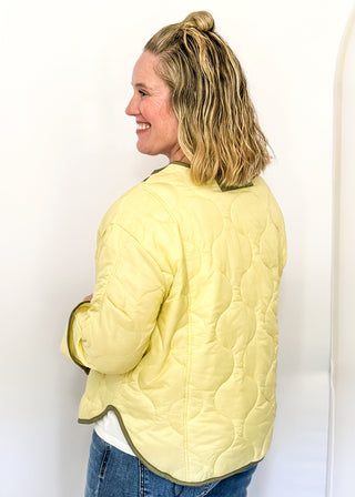 Light sage green quilted jacket with darker contrast trim, long sleeves, patch pockets, and button-front closure