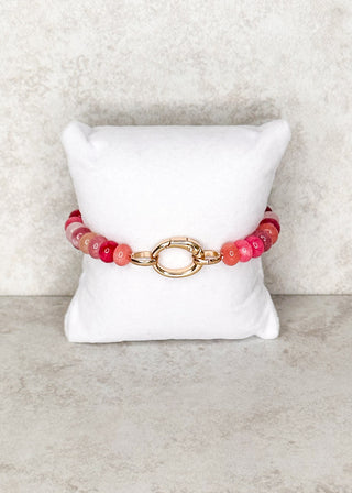 Pink beaded bracelet with large gold clasp displayed on stand.