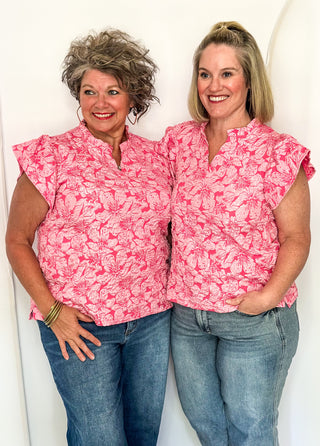 Two women wearing pink jacquard flutter sleeve blouses with a floral pattern, standing side by side.