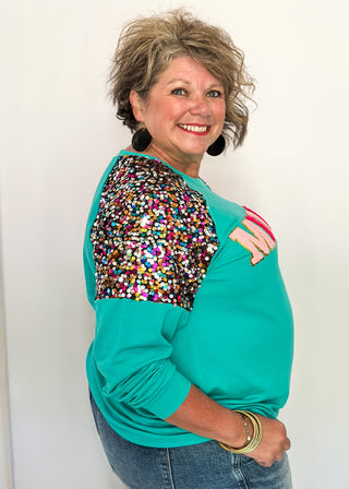 Turquoise long sleeve top with multi color sequin sleeves and chenille ‘MERRY’ lettering across the front.