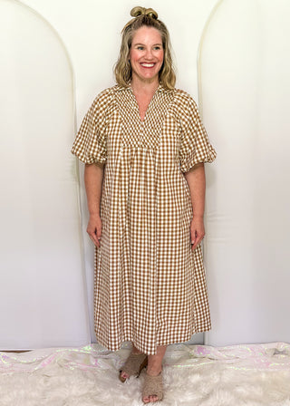 Woman wearing long brown gingham dress with short sleeves.