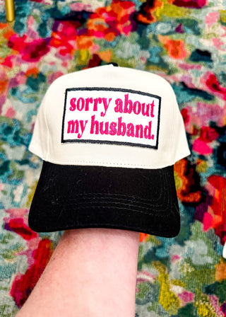 Cream snap back ball cap with a black bill and embroidered patch “sorry about my husband,” stitched in hot pink