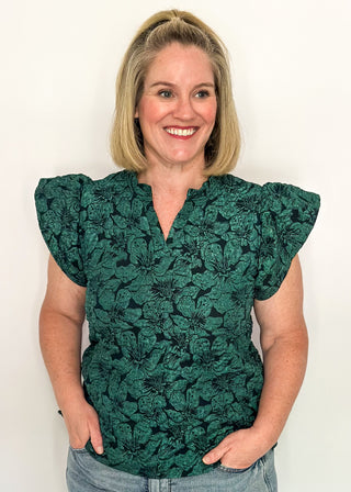 woman wearing forest green jacquard flutter sleeve blouse with a floral pattern