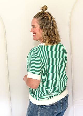 Woman wearing a green and white striped shirt and blue jeans against a white background