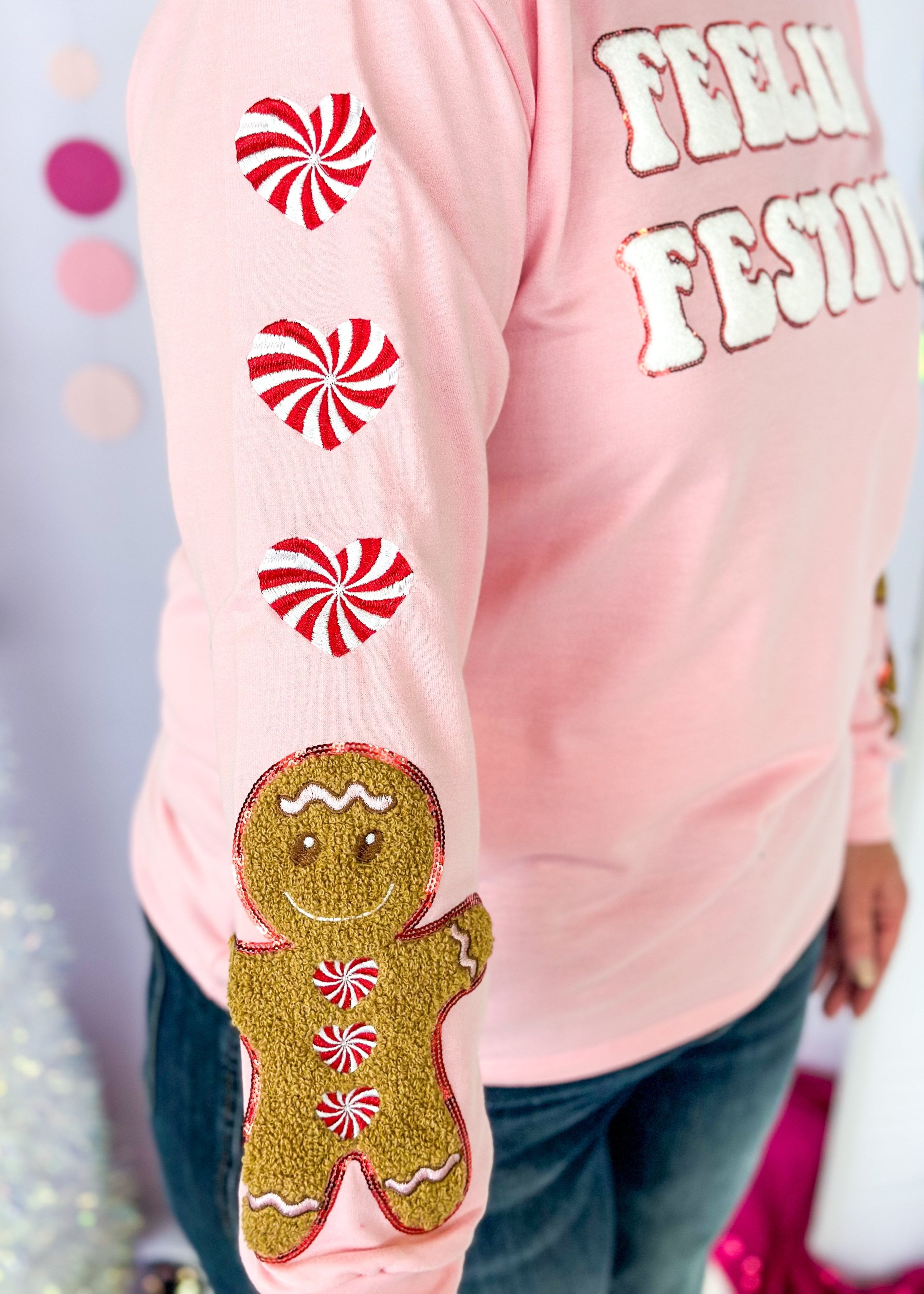 pink long sleeve top with feelin' festive patches across the front - heart shaped peppermint patches down the sleeve with one gingerbread man patch at the bottom of each sleeve