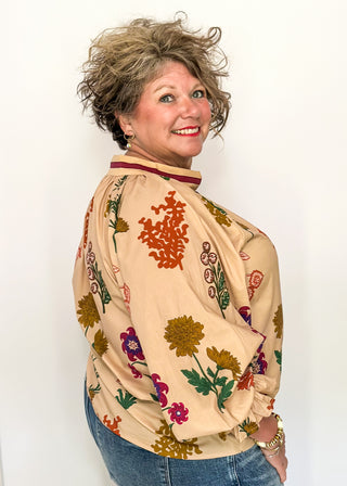Beige top with v-neckline, contrast trim, and vibrant floral design.