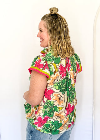 Bright floral blouse in pink, green, and yellow tones with split neckline and cap sleeves.