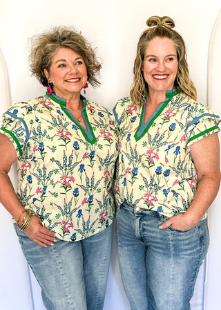 Cream short sleeve floral top with blue, pink, and green flowers, featuring a split V-neckline with green trim and a relaxed fit.