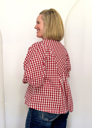 A woman with blonde hair stands with her back to the camera, wearing a red and white gingham shirt and blue jeans, posing in front of three large, white, dome-shaped inflatable or fabric panels in an indoor room.
