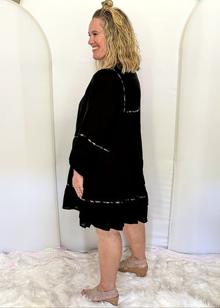 knee length black tiered dress with smocking on the chest and a tie closure at the rounded neck. 3/4 sleeve, leopard piping.