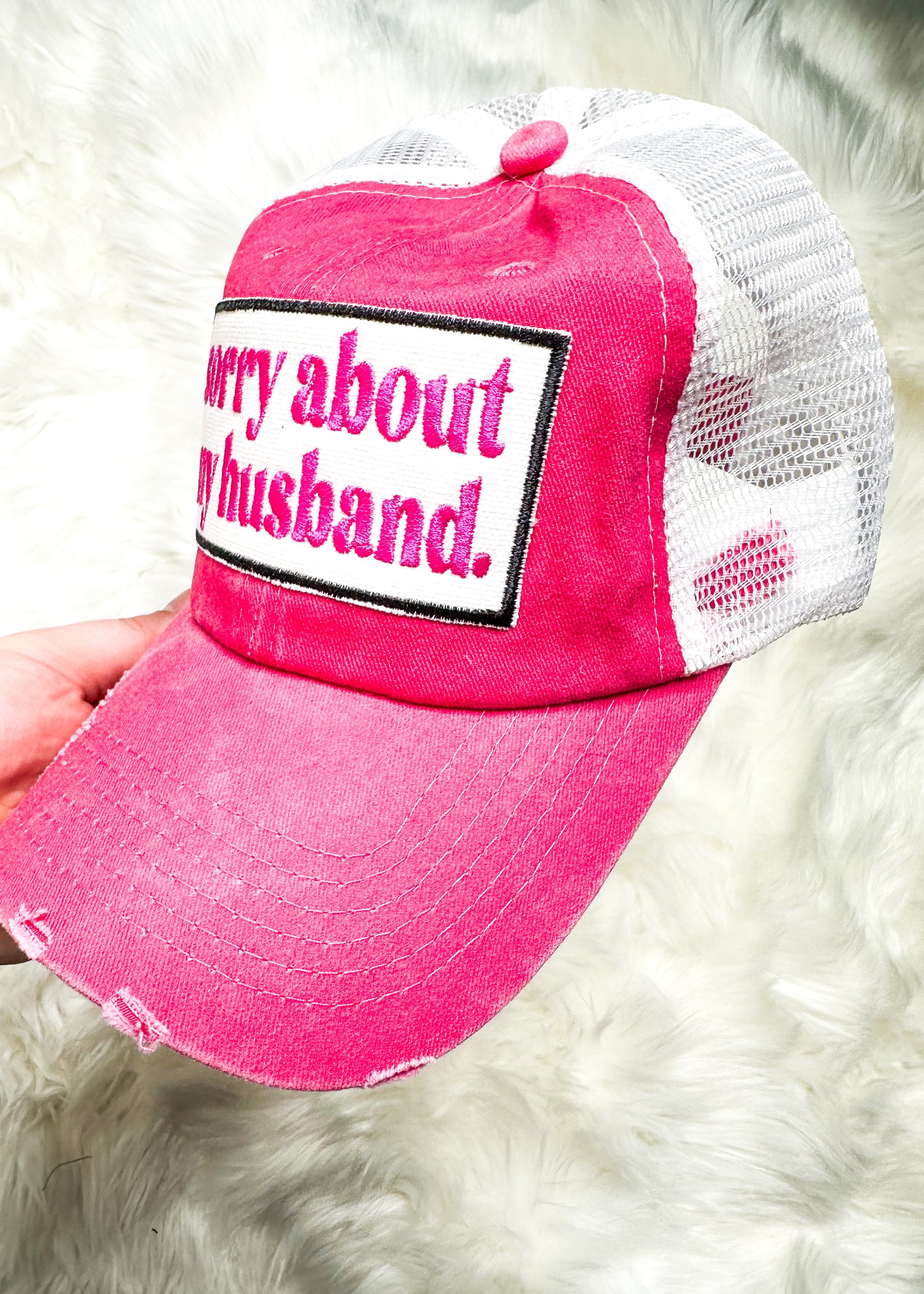 sorry about my husband embroidered in hot pink on white patch attached to a hot pink distressed trucker hat with white net back and velcro closure