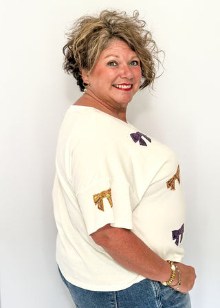 Short sleeve white top featuring scattered sequin bows in gold and purple