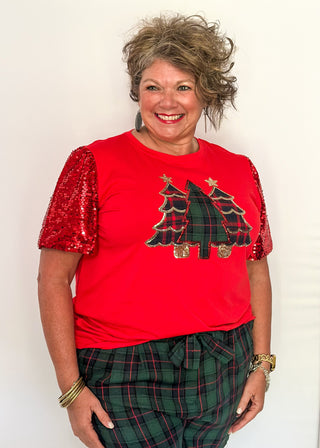 Person wearing a red shirt with tree design and sequin sleeves, standing against a white background.