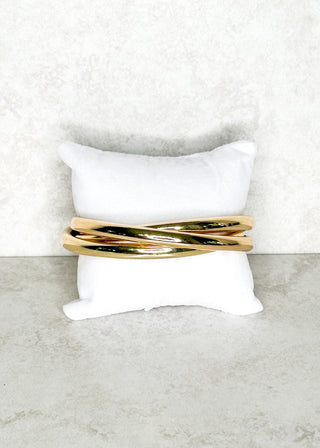 Gold bracelet on a white pillow with a light gray background