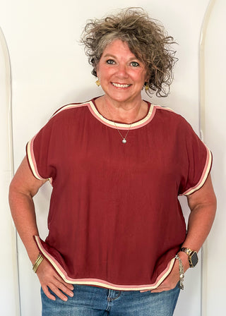 women wearing brick red top with cap sleeves and crew neckline, styled with jeans.