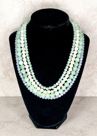 Multi strand beaded necklace in soft blue, green and white on a black neck form 