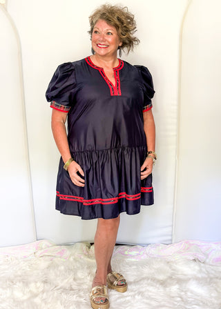 Navy puff sleeve dress with red plaid trim and tiered skirt.