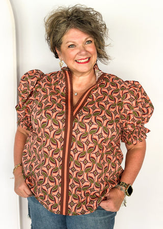 Bubble sleeve V-neck short sleeve top with terracotta, brown and green print. Ribbon detail down the front in brown and terracotta. 