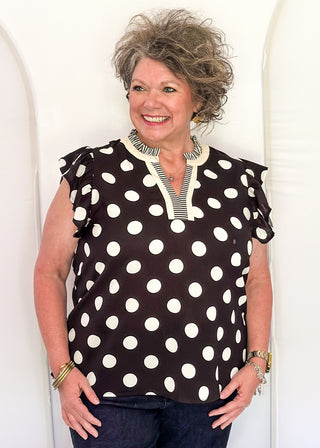 Women's black blouse with cream polka dots, striped split neckline, and flutter sleeves.