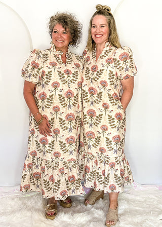 Two women wearing ecru midi dresses with floral patterns, standing side by side.