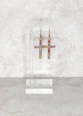 Colorful rhinestone cross fish hook earrings on a clear stand against a light gray marble background