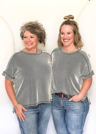 Two women wearing matching striped shirts and jeans standing against a white background