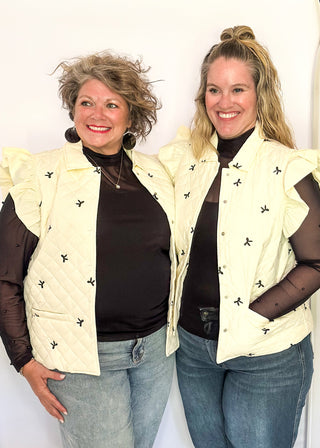 Ivory quilted puffer vest-ruffle sleeve, front pockets, snap closure. Small black bows embroidered throughout.  
