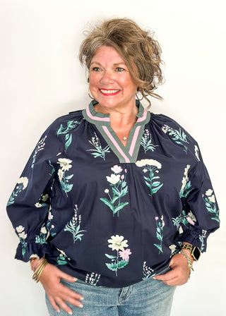 dark navy top with florals in light pink and white with green leaves.  3/4 length sleeve and v-neck with contrast detail in dusty blue and light pink. 