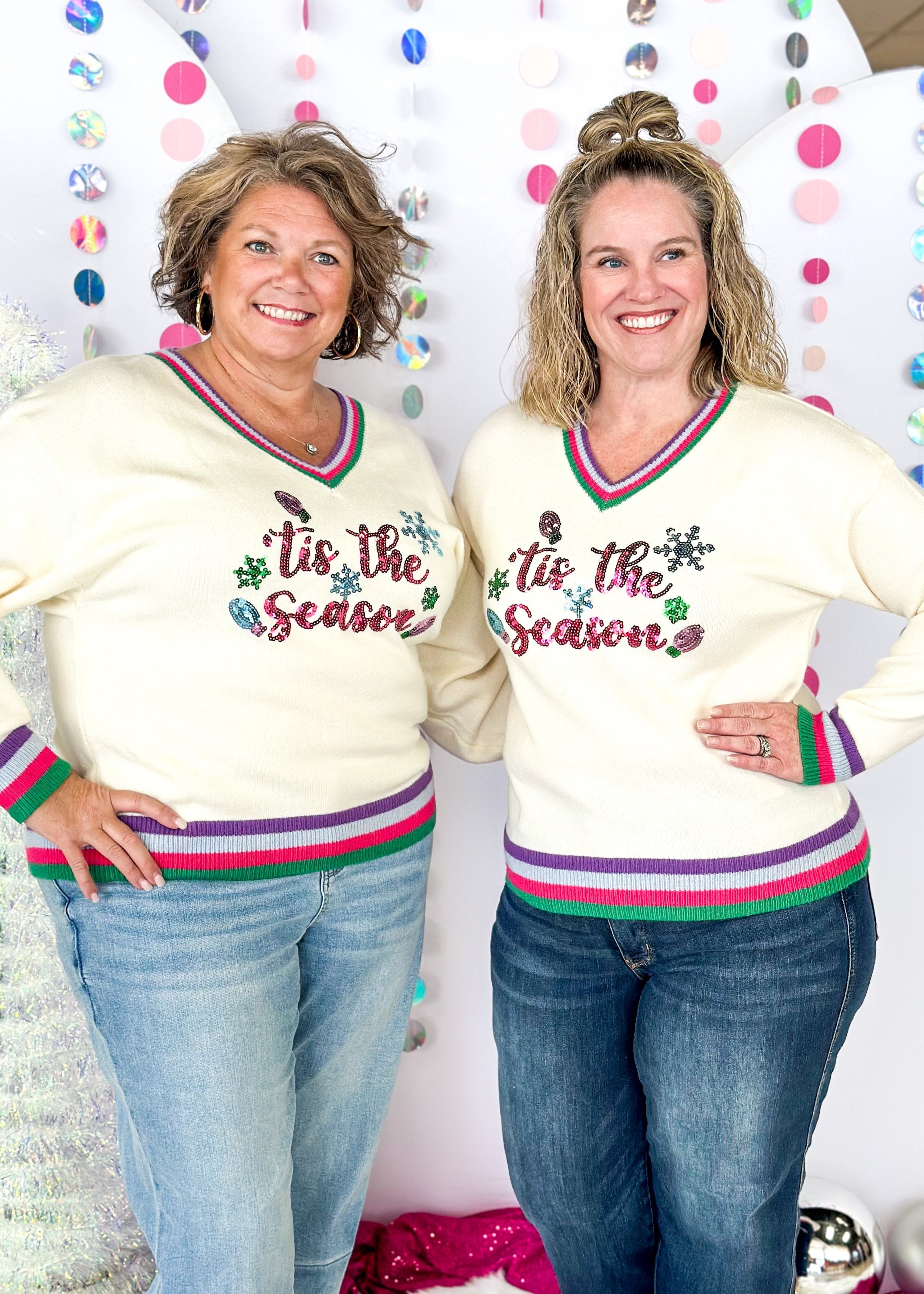 cream long sleeve sweater with v-neck, cuffs and bottom banding all striped in purple, pink, green and light blue, tis the season spelled out across the front in sequins