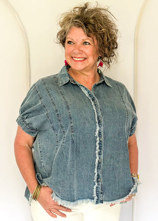 Denim button-down top with short sleeves, pointed collar, vertical stitched panels, and frayed raw-edge hem.