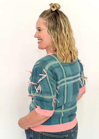 Turquoise plaid short sleeve sweater with pink trim and bow accents on the sleeves