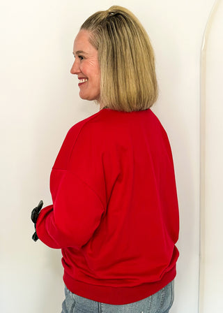 side view of woman wearing a red long sleeve top with Hunter Green contrast, velvet bows on sleeve and sequin lettering "fa La La La la"