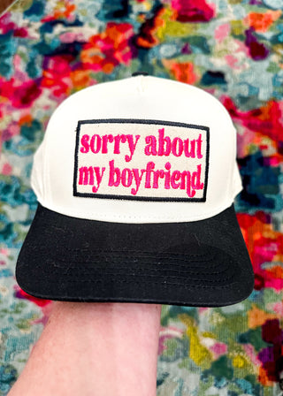Cream snap back ball cap with a black bill and embroidered patch “sorry about my boyfriend,” stitched in hot pink
