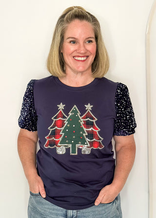 woman wearing a navy short sequin sleeve top with plaid and green embellished trees