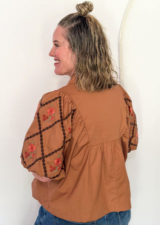 woman in chestnut poplin puff sleeve top with embroidery. 