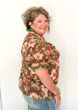 pink and golden botanicals on a brown background.  Short ruffle sleeves, v-neck ruffle collar in pink and green 