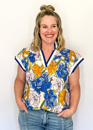 Floral top featuring blue, yellow, and lavender blooms with blue contrast trim on neckline and sleeves.