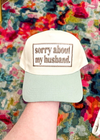 Cream snap back ball cap with a light green bill and embroidered patch “sorry about my husband,” stitched in kahki.