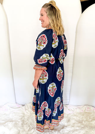 Navy maxi dress with colorful floral medallion print, orange embroidered trim at neckline, and smocked cuffs