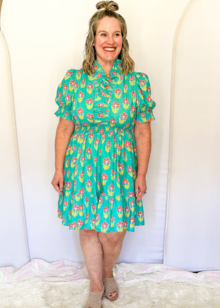 Mint green floral dress with colorful pink flowers, featuring short puff sleeves, ruffled neckline, smocked waist, and flowy skirt.