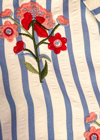 Close up of short sleeve button up top with blue stripes and embroidered floral bundles in red and pink. 