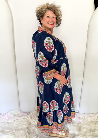 Navy maxi dress with colorful floral medallion print, orange embroidered trim at neckline, and smocked cuffs