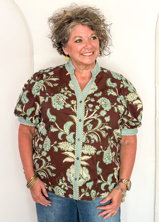 woman standing in a brown, cool blue and cream button up top and jeans.