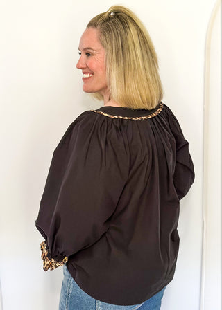 Black long-sleeve blouse with leopard print trim on split neckline and cuffs.