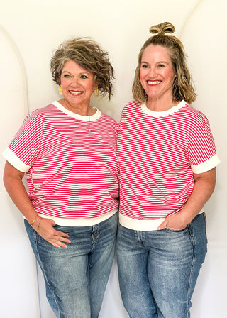 Two women wearing matching red and white striped shirts and blue jeans standing against a white background.