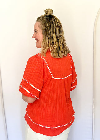Dark coral short sleeve blouse with puff sleeves, split V-neckline, textured fabric, contrast white stripe trim detailing.